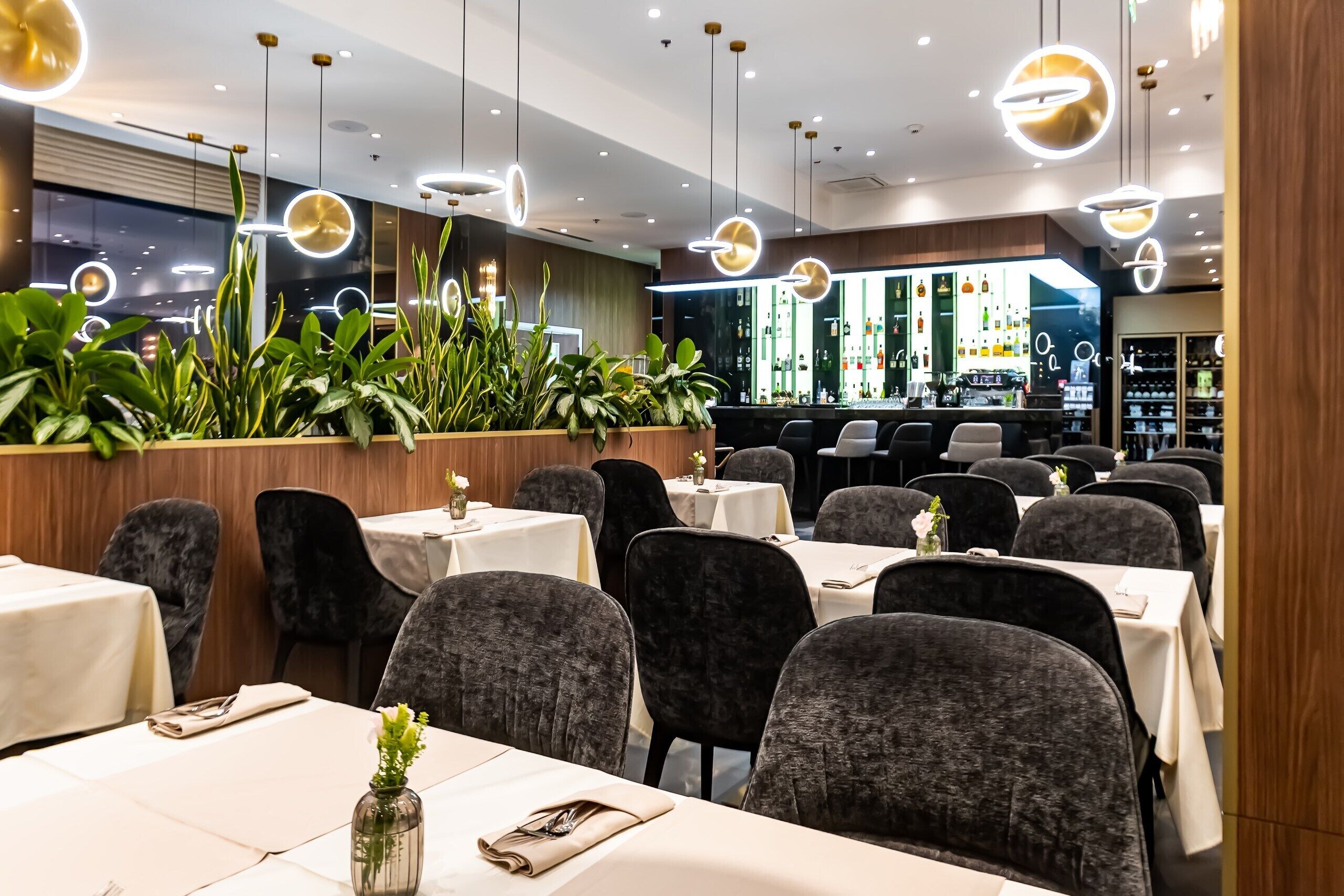 A restaurant with tables, chairs, hanging lights, and a bar area.