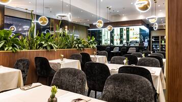 A restaurant with tables, chairs, hanging lights, and a bar area.