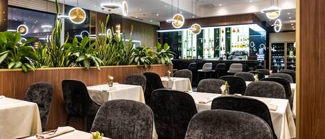 Un restaurante con mesas, sillas, luces colgantes y una zona de bar.