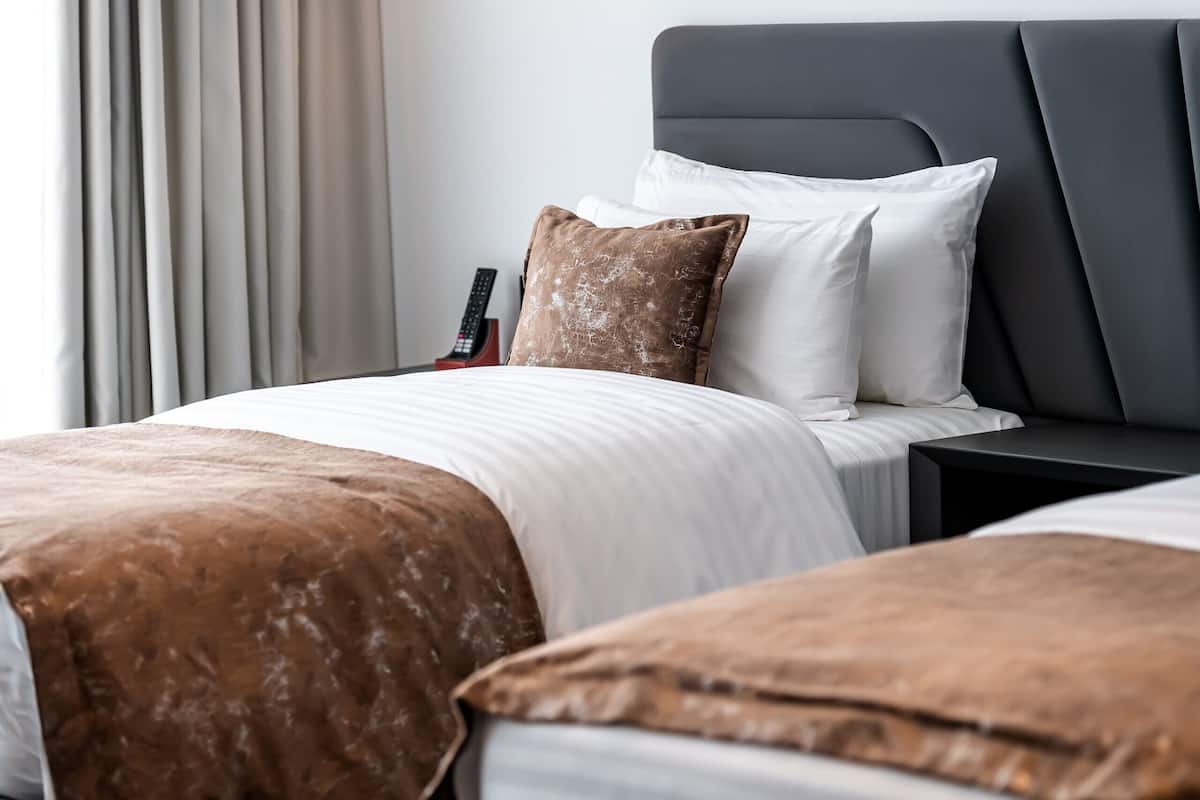 Una habitación de hotel con una cama, almohadas, una mesita de noche y un control remoto.