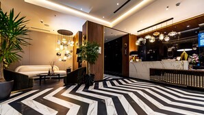 Un vestíbulo moderno con un estampado geométrico blanco y negro en el suelo, una recepción y una zona de estar con un sofá y una mesa de centro.