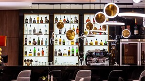 Zona de bar con estantes llenos de botellas de licor, una máquina de café y taburetes de bar.