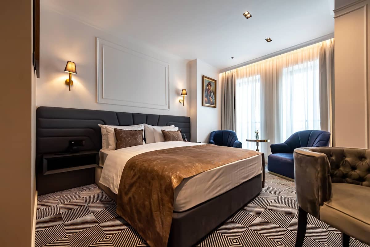 Habitación de hotel con una cama grande, dos sillones, una mesita y un cuadro en la pared.