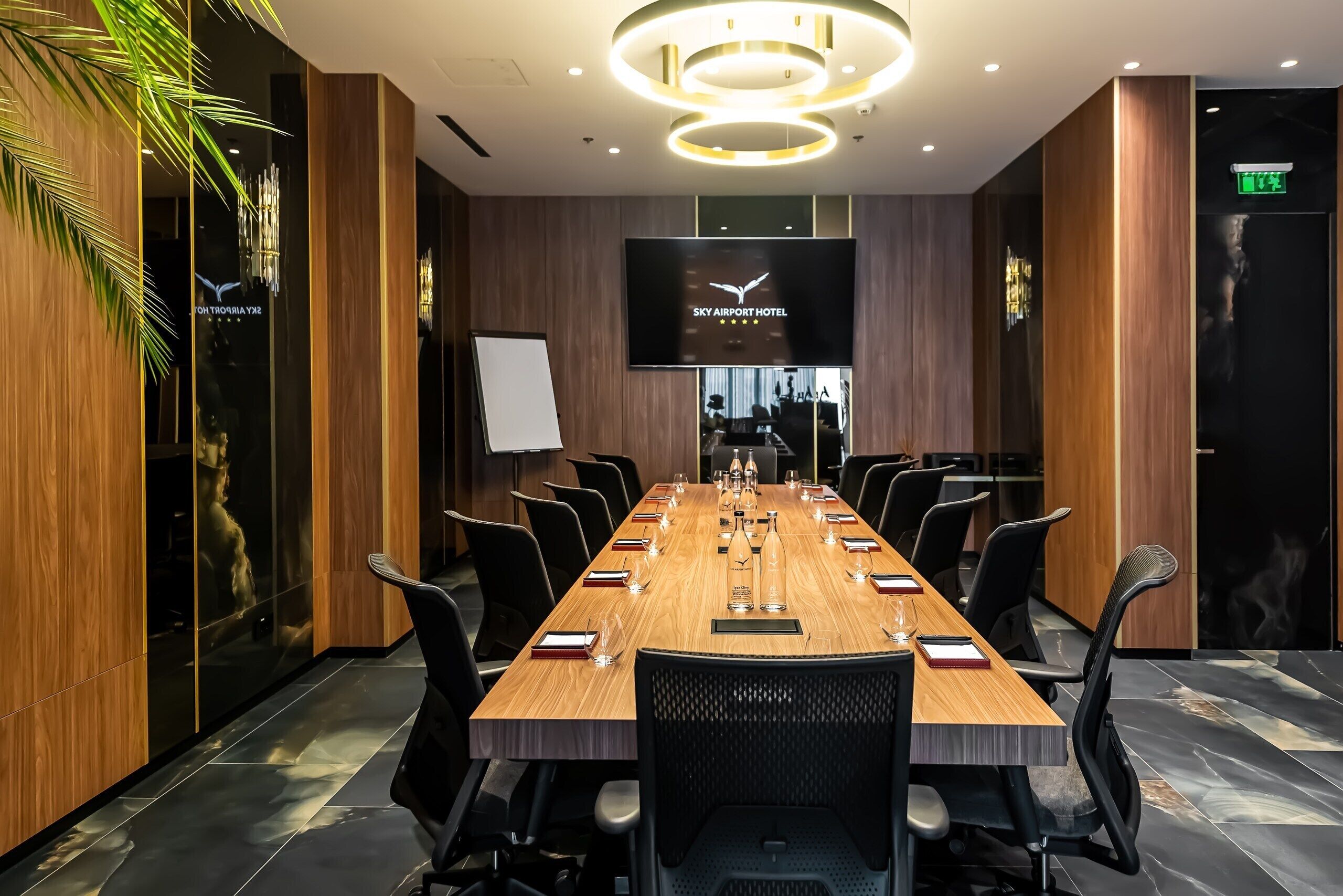 A conference room with a long table, chairs, a TV screen, and a wooden wall.