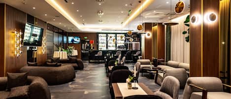 A modern hotel lobby with a bar area, seating arrangements, and a television screen.