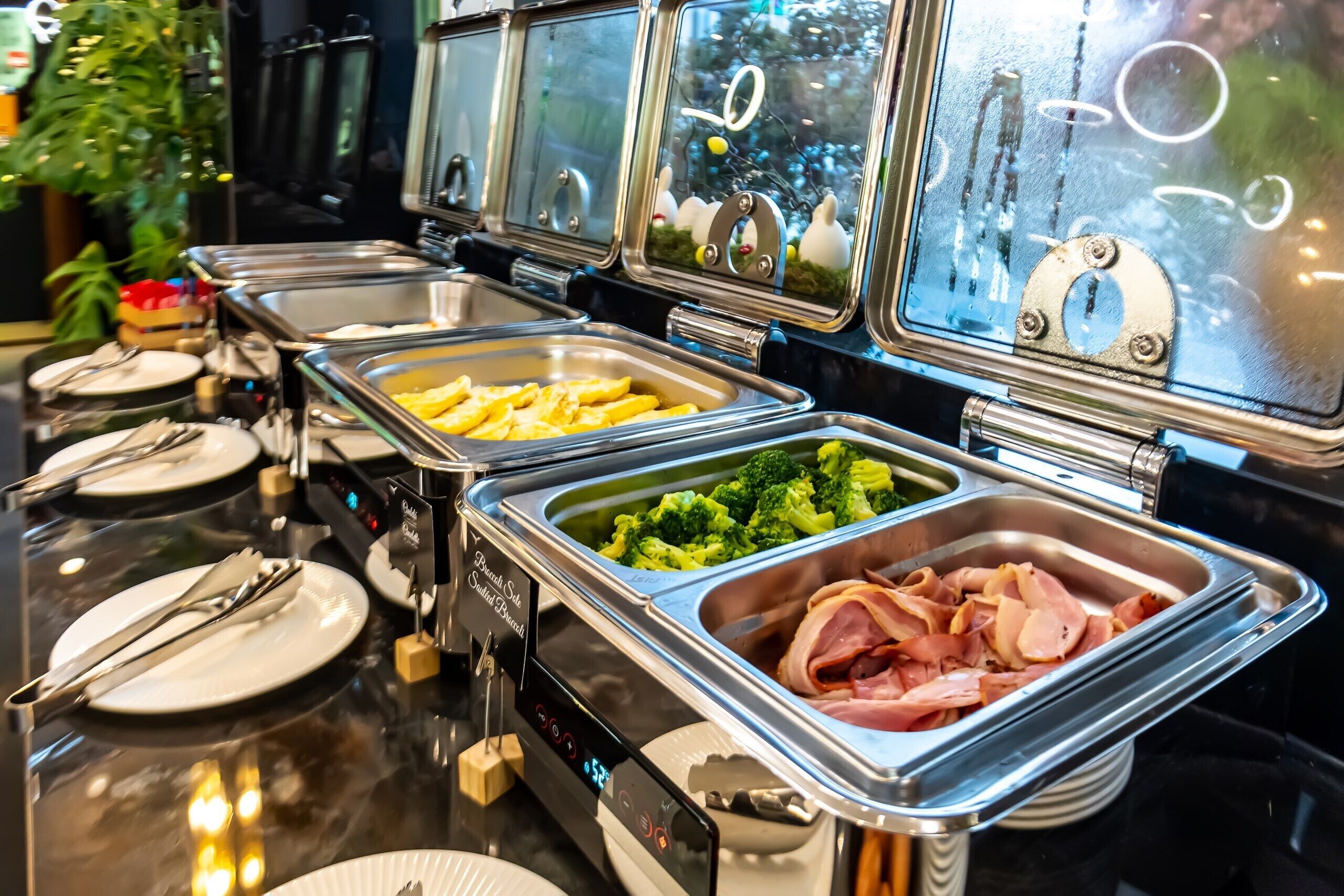 Un bufé con distintos alimentos, entre ellos brócoli, jamón y papas fritas.