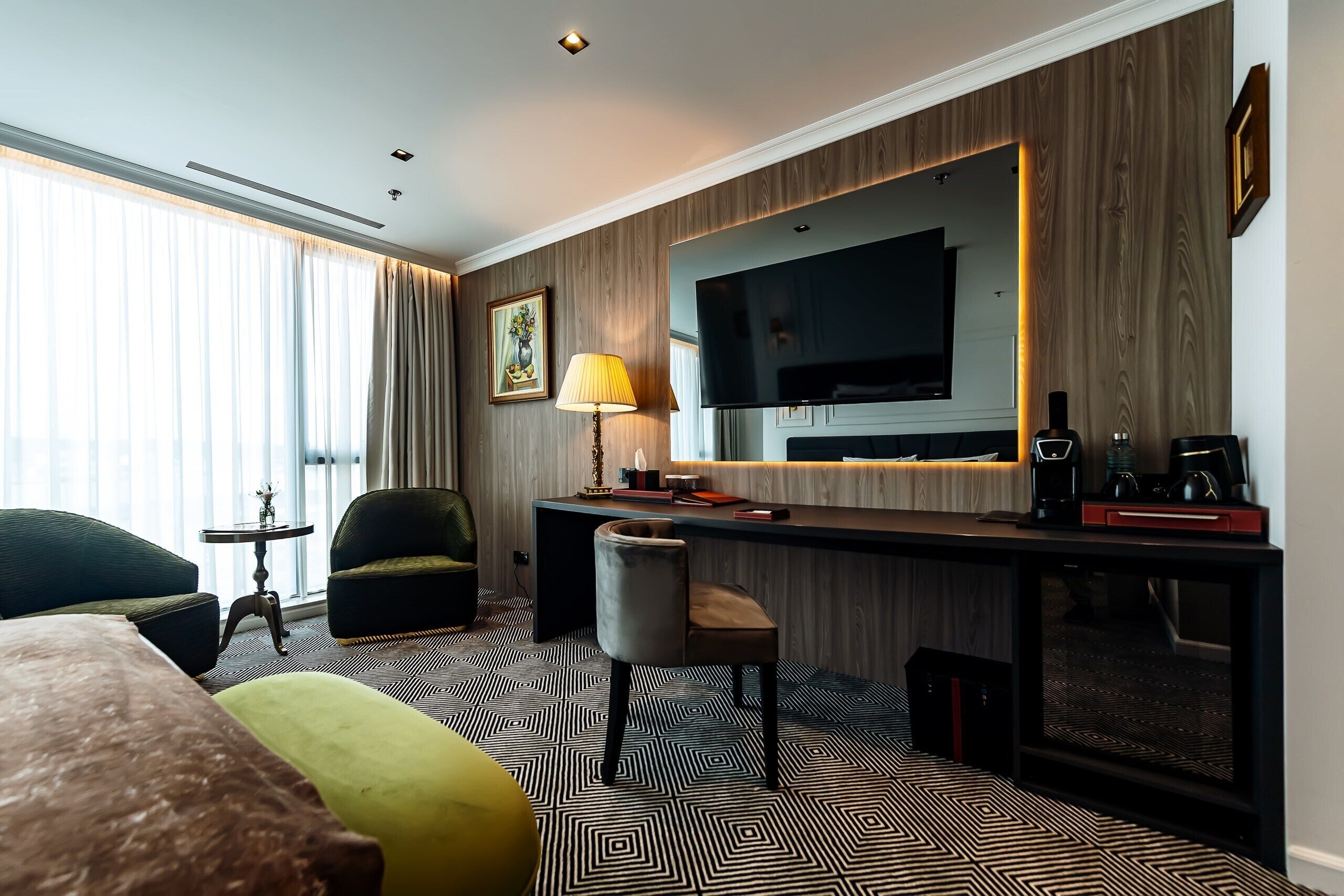 A hotel room with a bed, a desk, a chair, a TV, and a lamp.