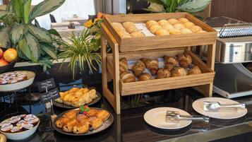 Een buffet met diverse gebakjes en desserts, waaronder croissants en broodjes, gepresenteerd op houten standaardjes.