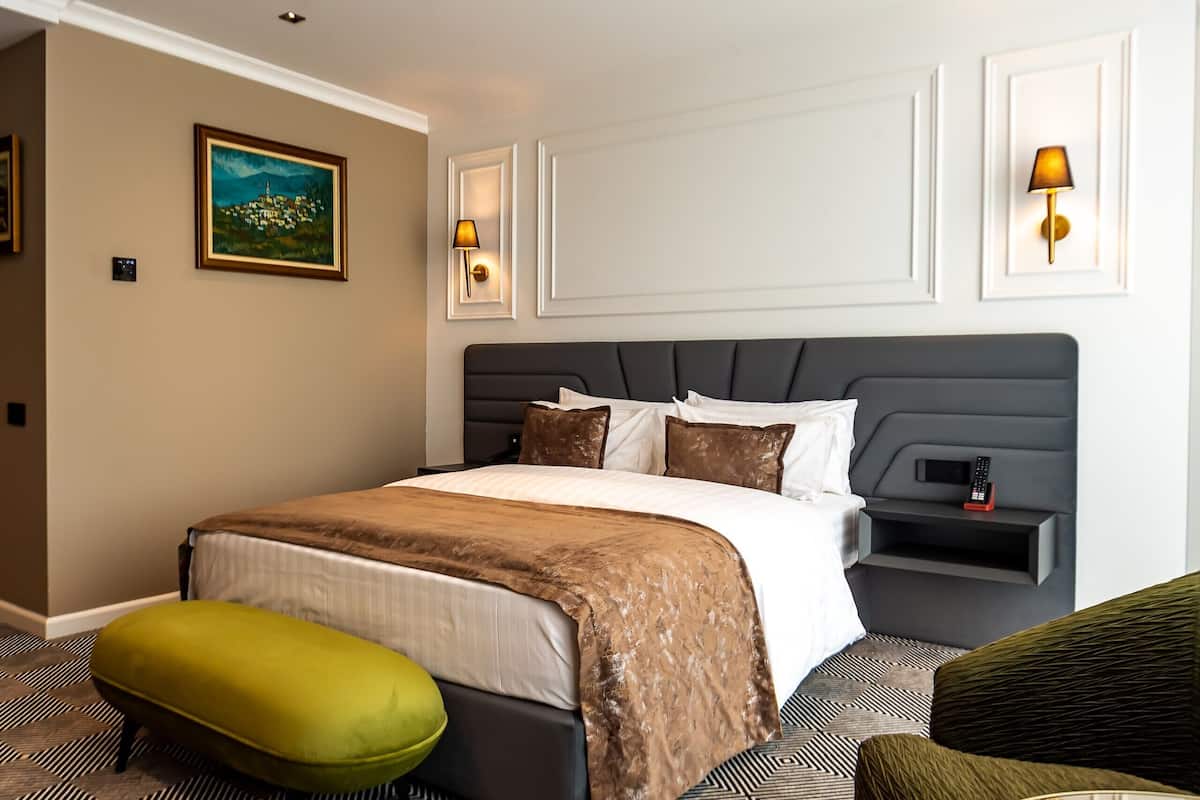 Una habitación de hotel con una cama grande, mesitas de noche, una silla verde y un cuadro en la pared.
