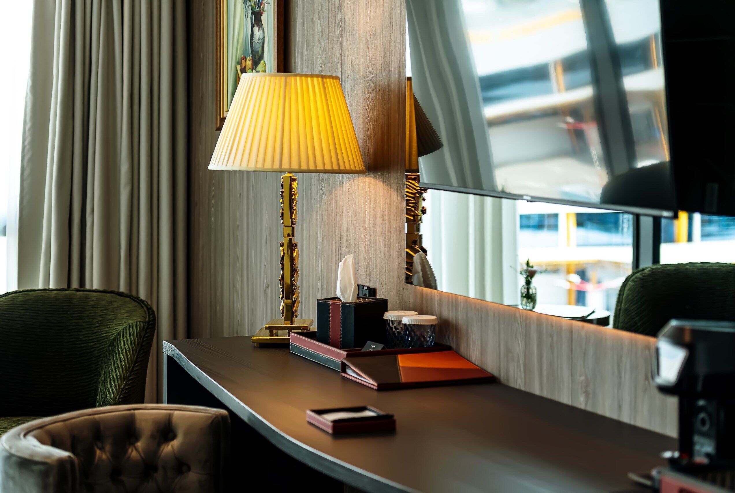 A hotel room with a desk, a lamp, a chair, and a view of the outside.