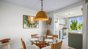 A dining area with a glass table, wicker chairs, and a hanging light fixture. - Princeville condo with ocean views, pool and hot tub access summer deals (PRINCEVILLE)