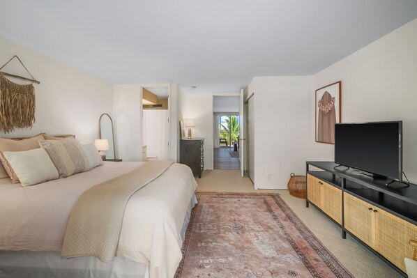 A bedroom with a bed, a TV, a console table, and a view of the outside. - Princeville condo with ocean views, pool and hot tub access summer deals (PRINCEVILLE)