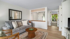 A modern living room with a grey sofa, a round wooden coffee table, and a large mirror on the wall. - Princeville condo with ocean views, pool and hot tub access summer deals (PRINCEVILLE)