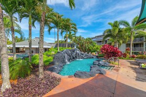 A resort pool area with a natural rock formation, palm trees, and a clear blue sky.