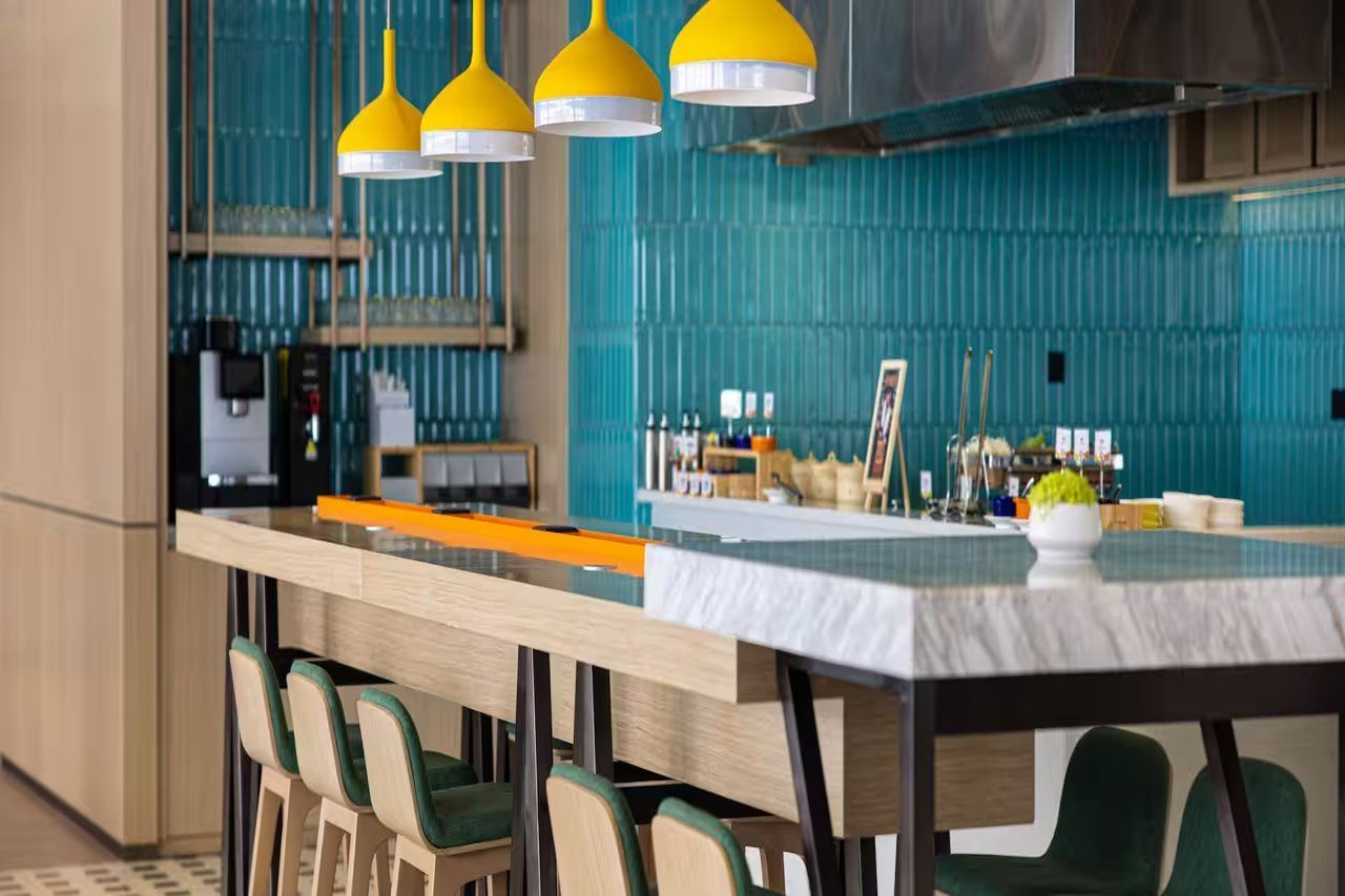 A modern kitchen with a central island, bar stools, and yellow pendant lights.