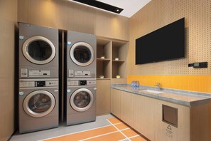 A modern laundry room with two Haier washing machines, a sink, and a flat-screen TV mounted on the wall. - Home2 Suites BY Hilton Wuhan Xudong (Wuhan)