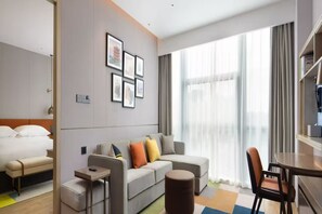 A hotel room with a bed, a sofa, a dining table, and a large window with curtains. - Home2 Suites BY Hilton Wuhan Xudong (Wuhan)
