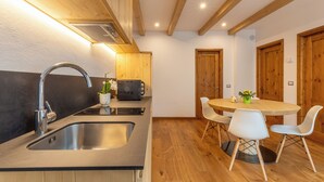 Eine moderne Küche mit Spüle aus Edelstahl, Holzschränken, einem runden Esstisch mit weißen Stühlen und Holzbalken an der Decke.