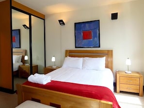 Habitación de hotel con cama, mesitas de noche, un espejo y un cuadro en la pared.