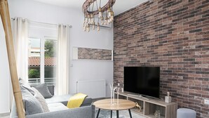 Een moderne woonkamer met een bakstenen muur, een flatscreen televisie, een houten salontafel en een bank met kussens.