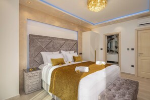 A modern bedroom with a large bed, a nightstand, a bench, a mirror, and an air conditioning unit.