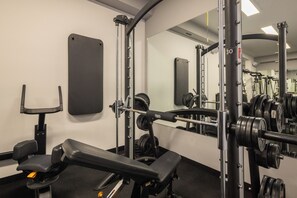 Een sportschool met gewichthefapparatuur, een bank en een spiegel.