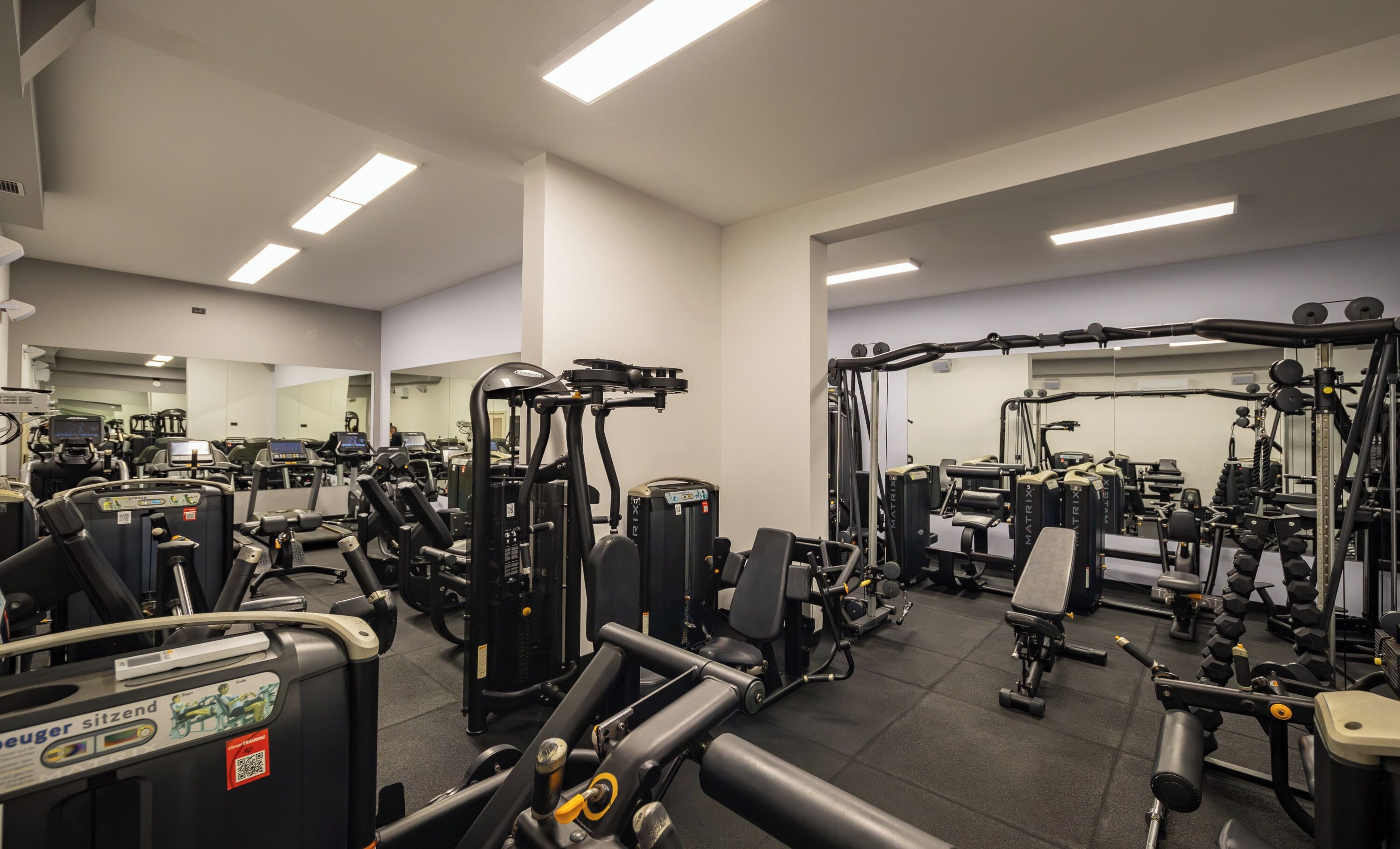 A gym with various exercise machines, mirrors, and a tiled floor.
