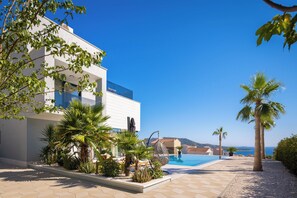A modern building with a pool, surrounded by palm trees and a clear blue sky.