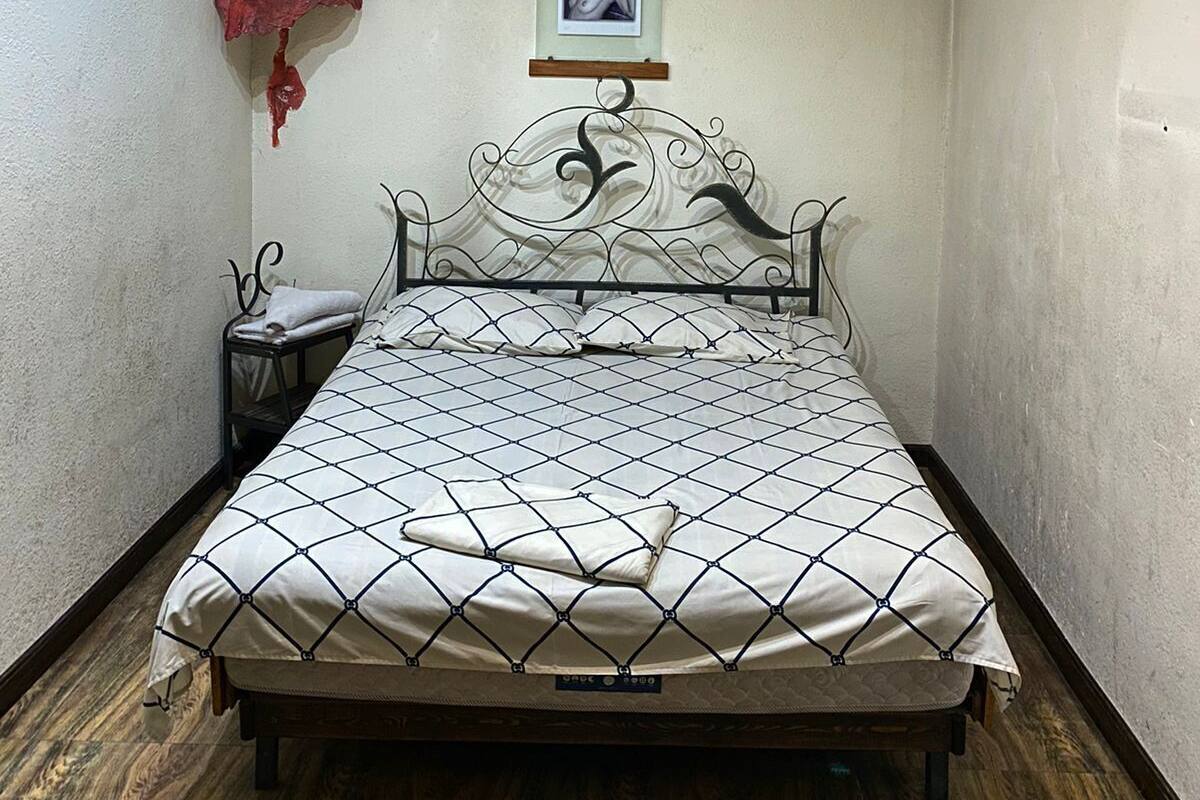 A bedroom with a bed, a nightstand, a wall-mounted shelf with a red object, and a framed picture.