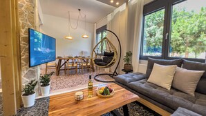 Ein modernes Wohnzimmer mit Steinwand, einem Holzesstisch, einem Hängesessel, einem grauen Sofa und einem an der Wand befestigten Fernseher.