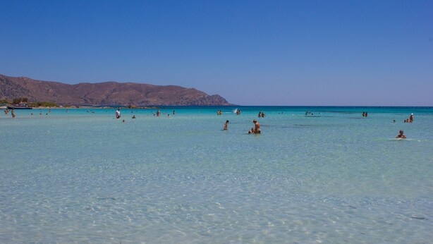 Ein Strand mit klarem türkisblauem Wasser und einer bergigen Kulisse.
