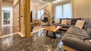 Ein modernes Wohnzimmer mit grauem Sofa, einem Hängesessel, einem Holztisch und einem Essbereich mit Tisch und Stühlen.