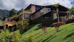 A modern two-story house with large windows, a balcony, and a well-maintained garden with various plants and flowers.