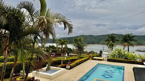 A pool area with a view of the sea and hills, surrounded by palm trees and well-maintained landscaping.