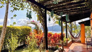 A covered outdoor area with a hammock, a stone wall, and a view of a body of water and mountains.