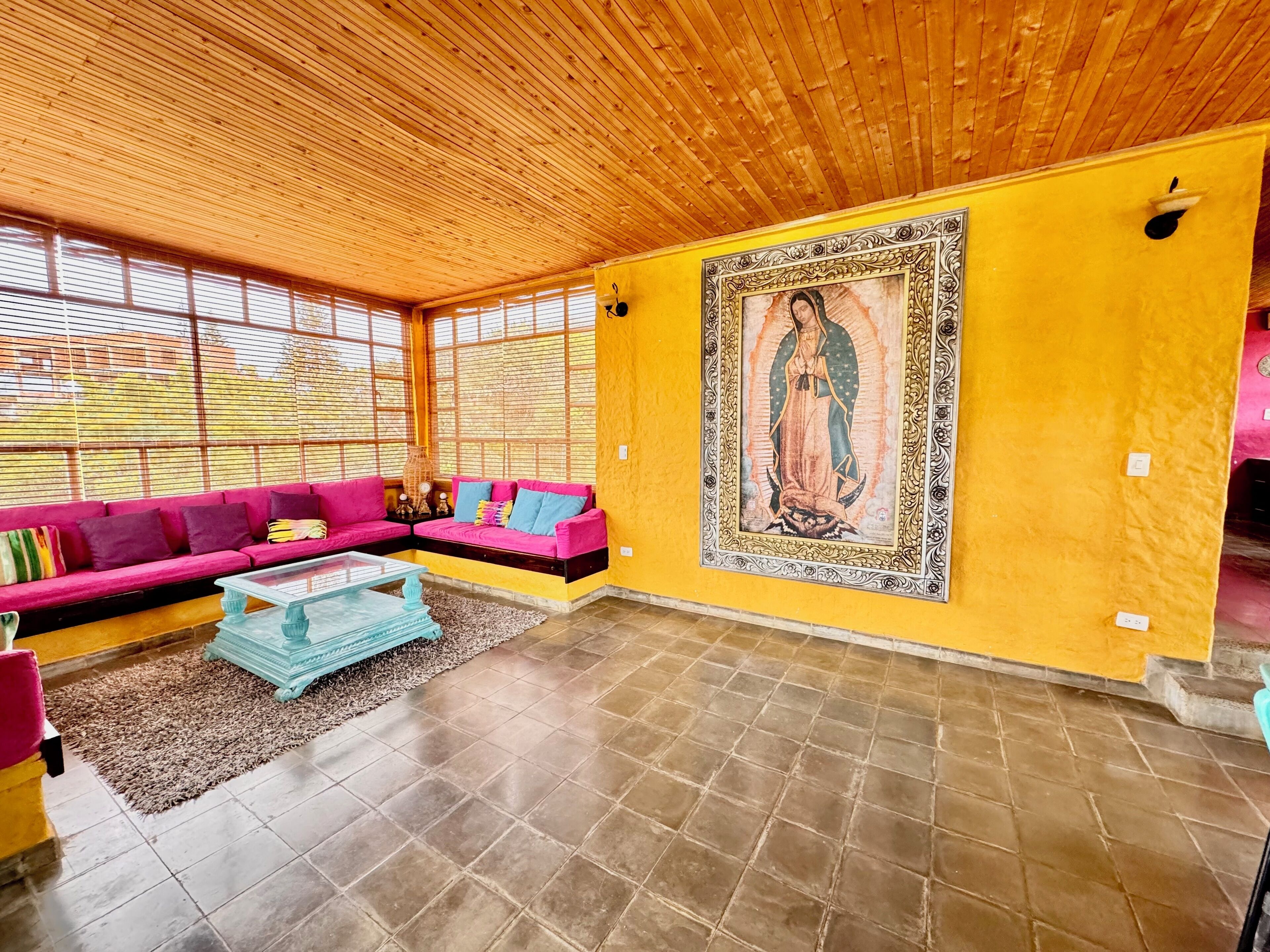Una habitación con techo de madera, sofá rosa, una mesa de centro de cristal y un cuadro grande enmarcado en la pared.