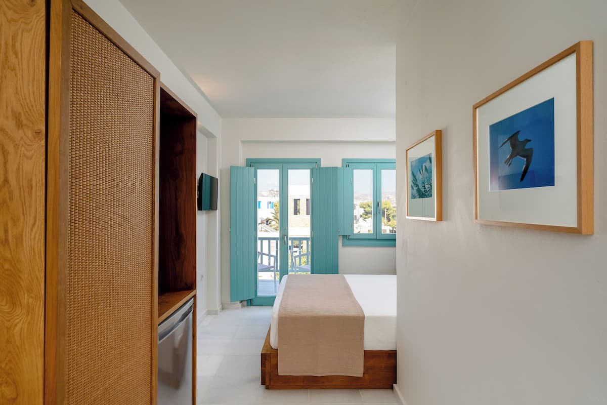 A bedroom with a bed, a wooden wardrobe, a woven partition, and a door leading to an outdoor area.