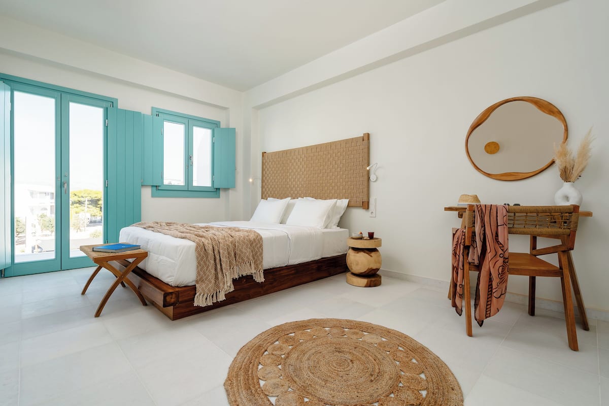 A bedroom with a bed, a bedside table, a chair, a round mirror, and a view of the outside.
