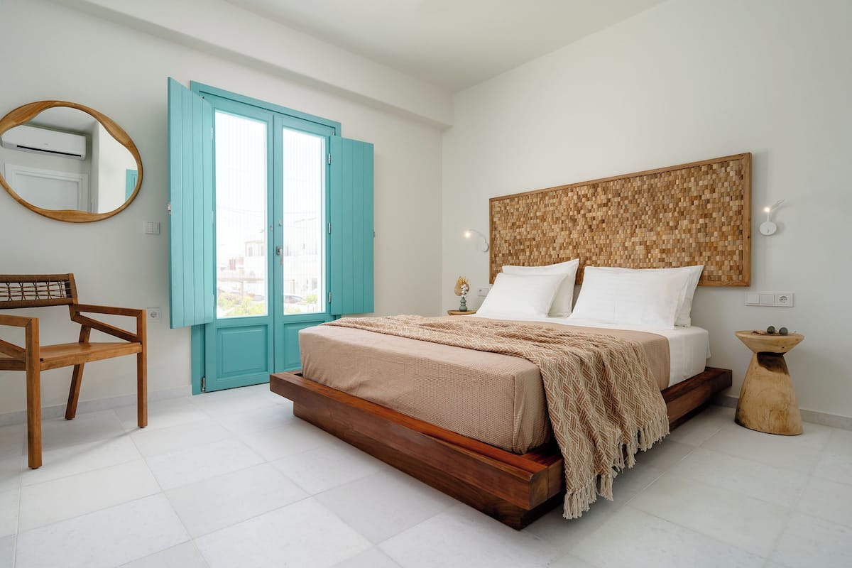 A bedroom with a wooden bed, a chair, a turquoise door, and a wall-mounted mirror.
