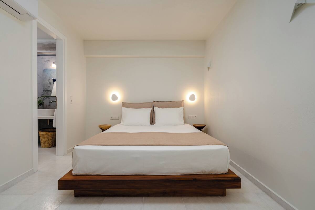 A minimalist bedroom with a bed centered in the room, two bedside lamps, and a small bedside table.