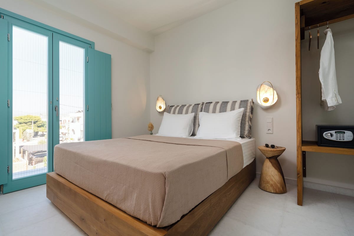 A bedroom with a bed, a wooden bedside table, a wall-mounted lamp, and a view through a door.