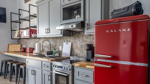 A modern kitchen with a red Galanz refrigerator, stainless steel appliances, grey cabinetry, and a wooden countertop. - Waylon In The Hill Country - Hacienda Amor (Johnson City)