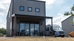 A modern two-story building with a flat roof, large glass windows, and a covered outdoor seating area with chairs. - Waylon In The Hill Country - Hacienda Amor (Johnson City)