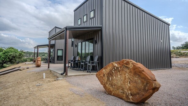 A modern building with a large rock in the foreground, a covered outdoor seating area, and a clear sky. - Willie In the Hill Country - Hacienda Amor (Johnson City)