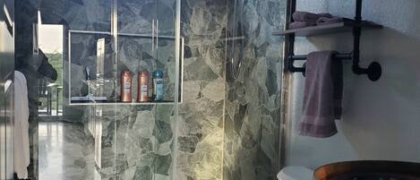 A bathroom with a stone wall, a glass shower enclosure, a toilet, and a wooden barrel.