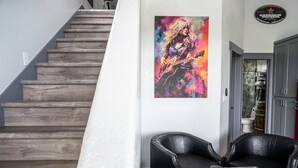 Un escalier avec des marches en bois, une affiche d’un musicien de rock accrochée au mur et une table basse en verre sur laquelle sont posés divers objets.