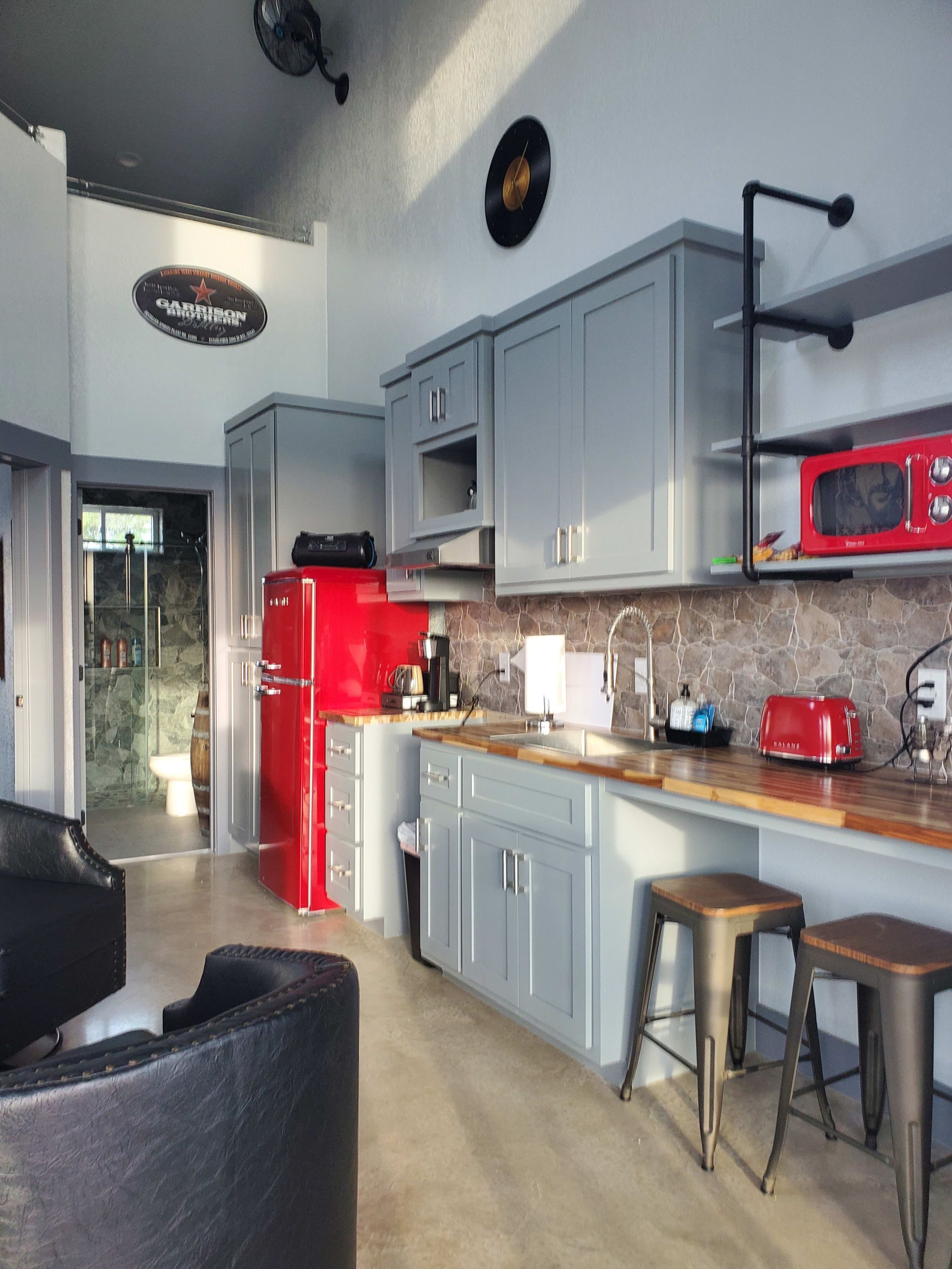 A modern kitchen with grey cabinets, a red refrigerator, a microwave, and a coffee maker. There is a stone backsplash and a wooden countertop.