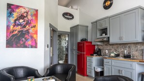 Une cuisine moderne avec des meubles gris, un réfrigérateur rouge et une machine à café. Il y a un tableau au mur et une table en verre avec des chaises.
