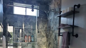 Un baño con pared de piedra, cabina de ducha de vidrio, inodoro y un barril de madera.