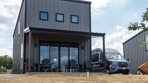 A modern two-story building with a flat roof, large sliding glass doors, and a covered outdoor seating area with chairs. - Stevie Ray In The Hill Country - Hacienda Amor (Johnson City)